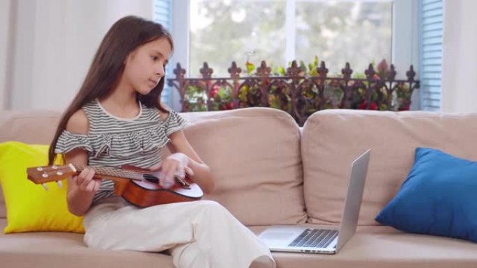 快乐的小孩在家看笔记本电脑时学习弹吉他。实时