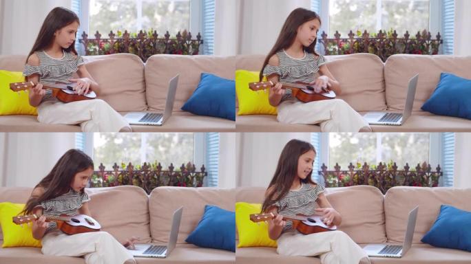 快乐的小孩在家看笔记本电脑时学习弹吉他。实时