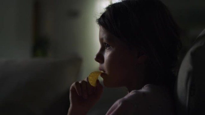 一个小女孩晚上在客厅看电视和吃薯条的特写肖像。女童专注于针对儿童的教育电视节目，学习新的事实和单词