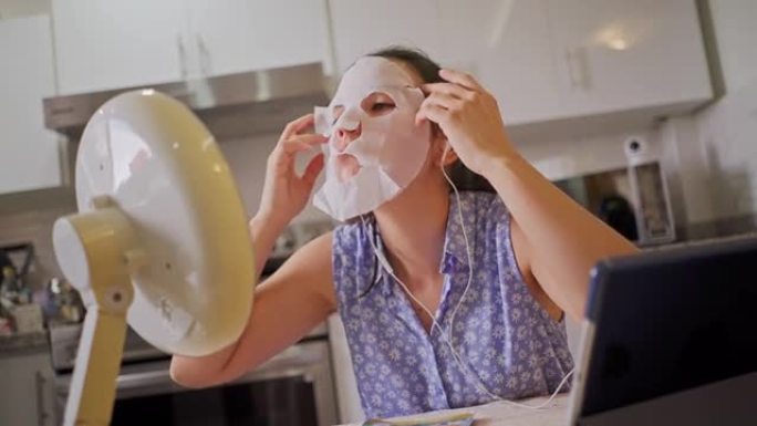 视频通话中的西班牙裔年轻女子在厨房里看着镜子时，设置了保湿、营养、透明质酸和祛痘的面膜