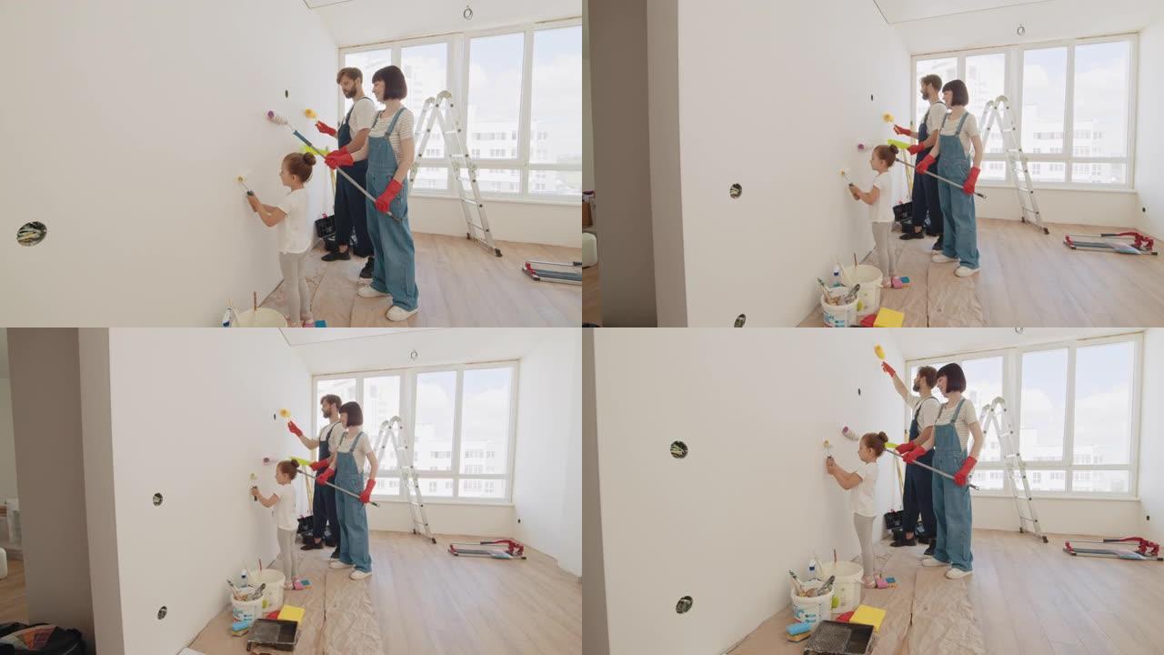 年轻的父亲和母亲向孩子展示如何用滚筒粉刷墙壁。油漆颜色为浅蓝色。家里的房间准备装修。公寓里的维修。一