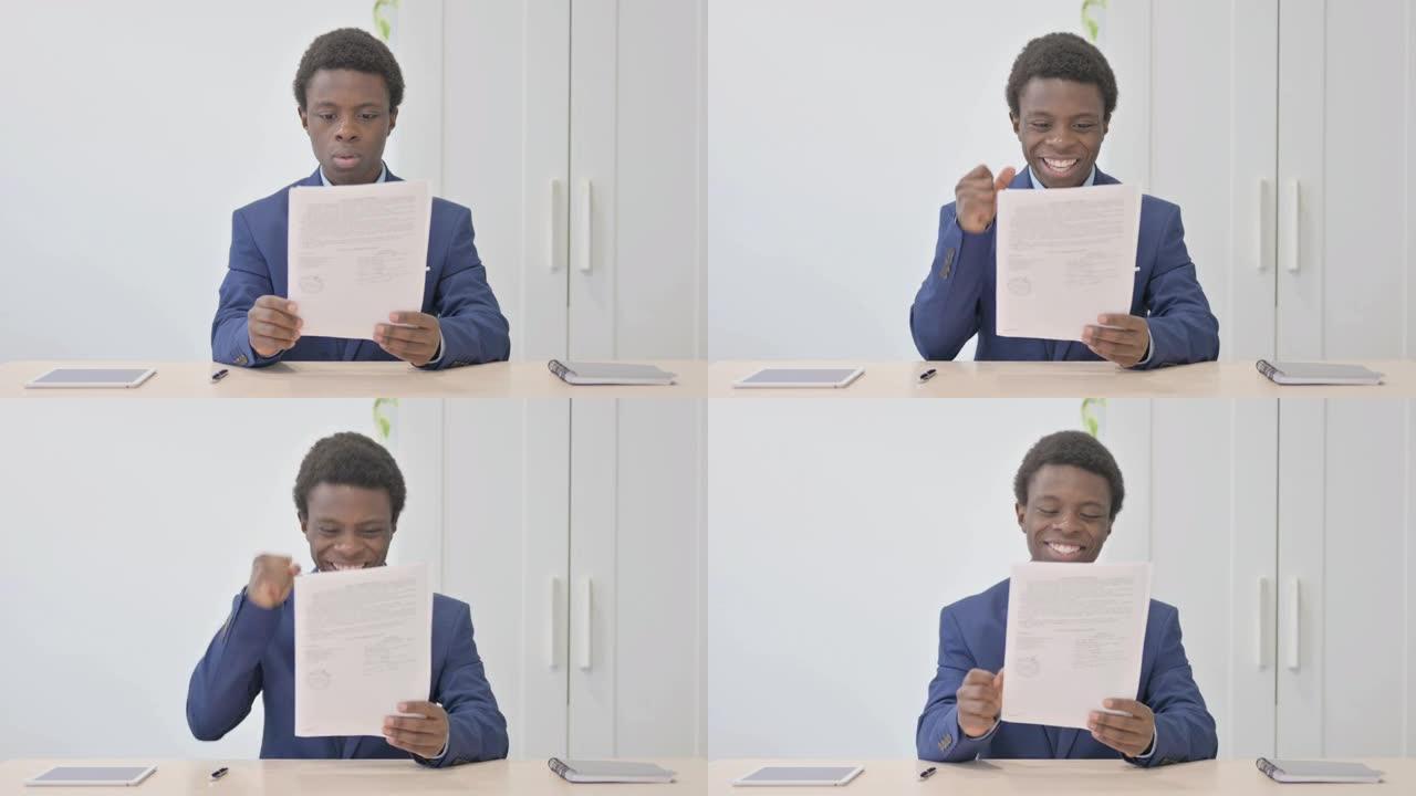年轻的非洲商人在办公室阅读文件时庆祝成功