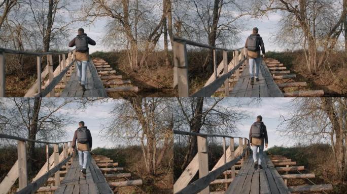 男子在傍晚的阳光下沿着河上的木吊桥行走，享受秋天的风景