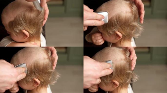 孩子的发型。理发师用理发推子剪小男孩。蹒跚学步的孩子第一次理发。父亲在家给他的小儿子剪头发。男婴在理