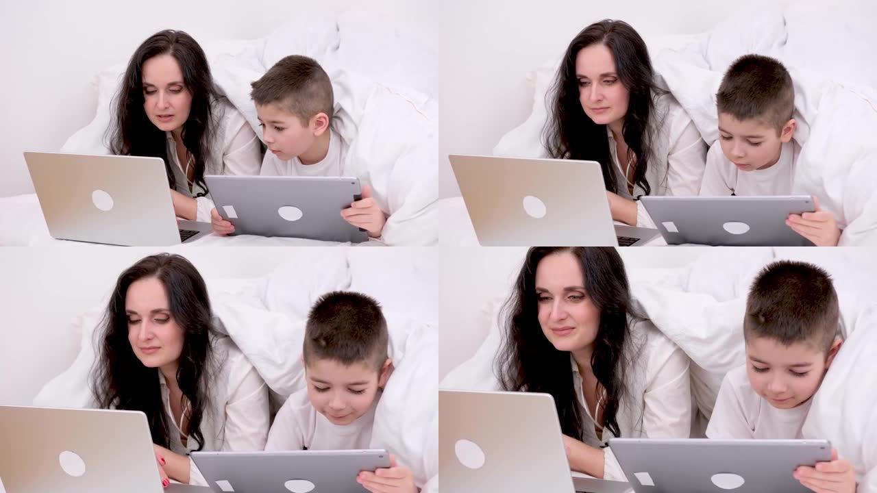妈妈和儿子躺在卧室的被子下照顾在线学习英语课程学习技术了解平板电脑笔记本电脑移动应用社交网络家庭我的