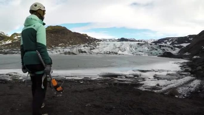 带有斧头和冰爪的女性徒步旅行者望着冰川
