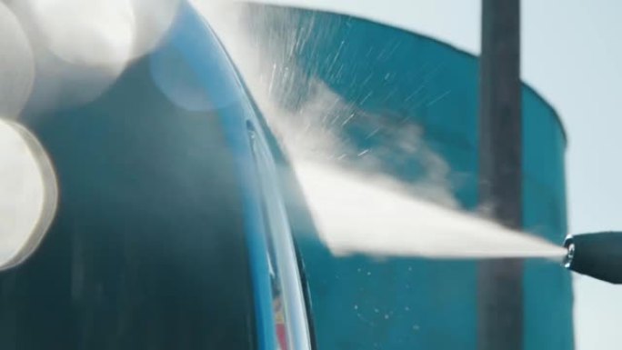 一辆蓝色拖拉机的车身正在慢动作清洗。水滴散落在周围。男子手持高压清洗机4K