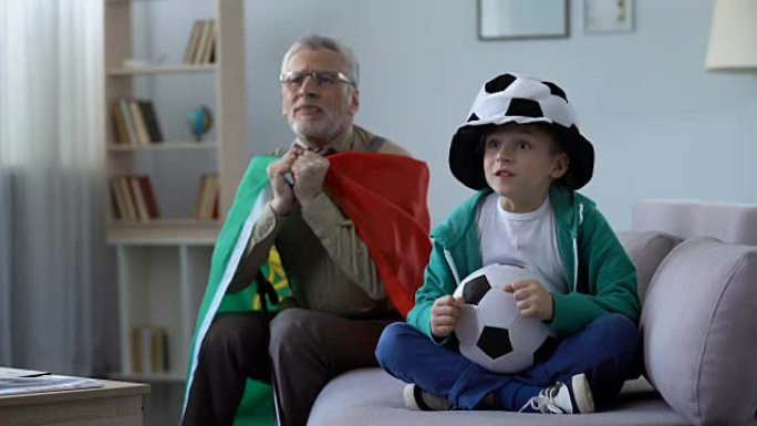 老人挥舞葡萄牙国旗，和孙子一起在家看足球