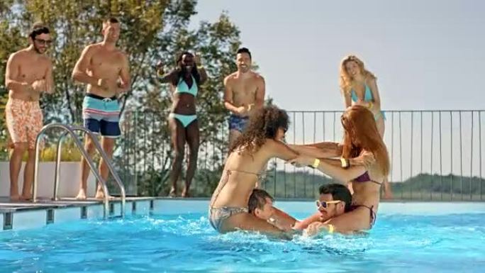 SLO MO DS两个女人在游泳池里打架，他们的朋友站在游泳池旁为他们加油