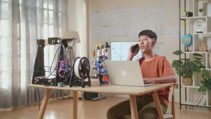 亚洲男孩在家里的笔记本电脑上工作时在智能手机上聊天