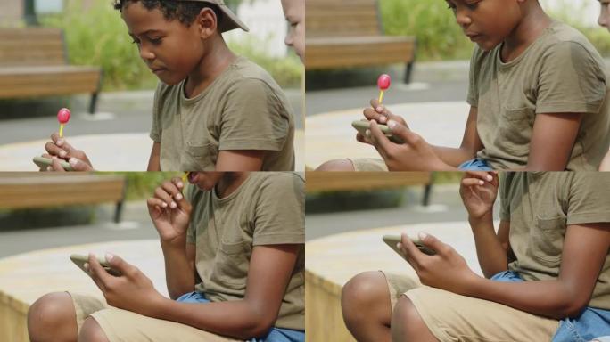 年轻的非洲裔美国男孩在公园的智能手机上观看视频