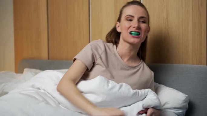 一个有魅力的女人在晚上睡觉前使用多功能训练器。它们有助于对准正在生长的牙齿并纠正咬合。纠正舌头的位置