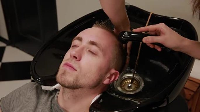 一个女人在理发店洗头，留着胡须的男人用洗发水和护发素。洗掉洗发水水