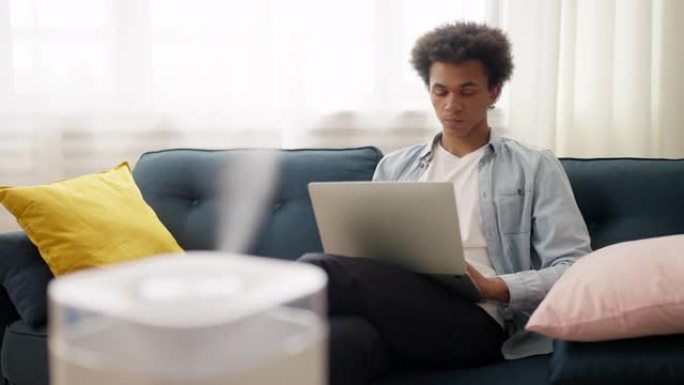 年轻的非洲裔美国人在家里使用笔记本电脑时使用空气加湿器