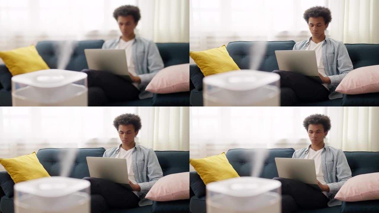 年轻的非洲裔美国人在家里使用笔记本电脑时使用空气加湿器
