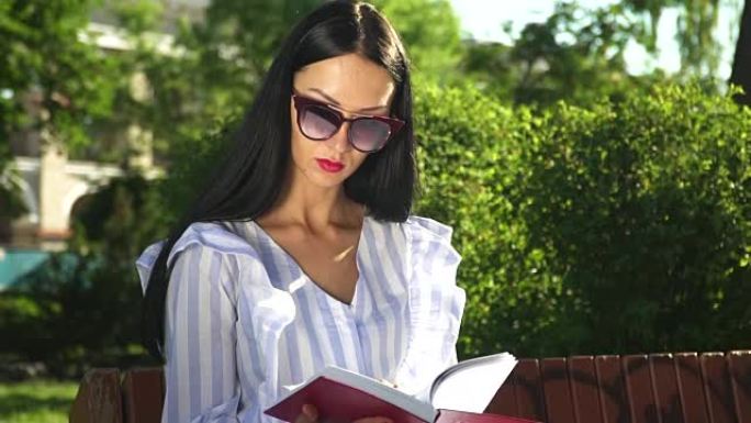 时尚的女人在太阳镜和脱衣阅读在夏季公园
