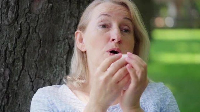 50多岁的金发女人在夏季公园休息时打喷嚏，过敏，鼻炎