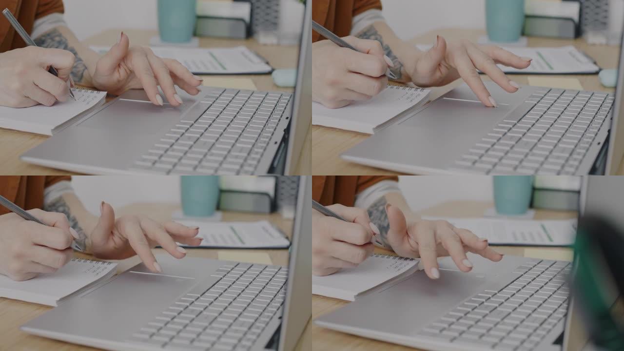 使用笔记本电脑和笔记本电脑在办公桌上书写信息的纹身手的特写镜头