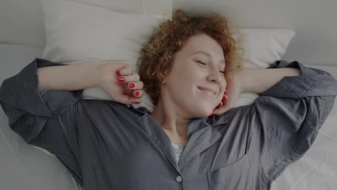 顶视图肖像迷人的红发女人雀斑醒来在床上伸展和微笑