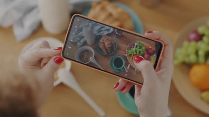 使用智能手机拍摄食物平放在厨房桌子上的女性手的特写
