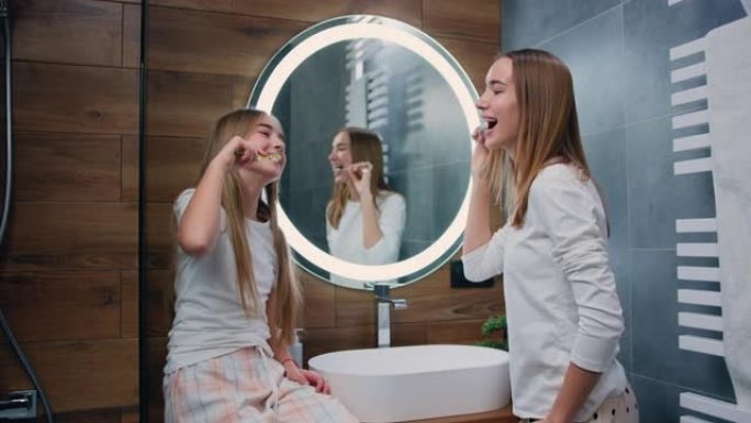 白人年轻和孩子姐妹刷牙微笑着看着对方。早上在浴室里微笑的女人和孩子照顾牙齿健康。