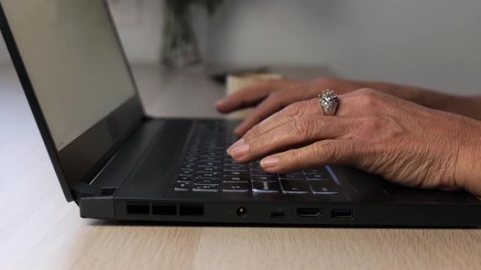一个老女人在笔记本电脑上打字的手的特写。