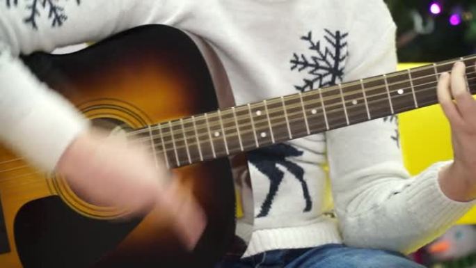 一个穿着灰色毛衣的年轻人弹着原声吉他。特写视频拍摄
