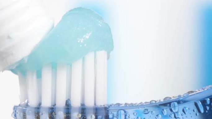 牙刷和牙膏。蓝白色背景上挤压牙膏的水滴蓝色牙刷的宏观视图。慢动作视图