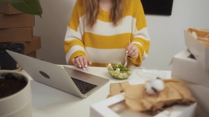 无法识别的女商人在工作中节食吃沙拉，企业家女性在午餐时在家庭办公室用笔记本电脑工作