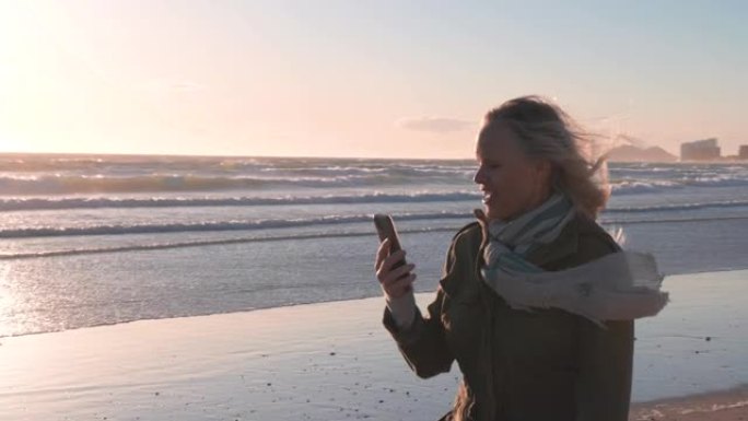 成熟的女人沿着空旷的海滩散步，在电话上聊天