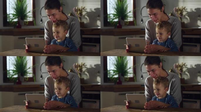 母亲和儿子在家里的厨房里用数字平板电脑拍摄的真实照片。男性蹒跚学步的孩子在享受零食的同时学习如何使用