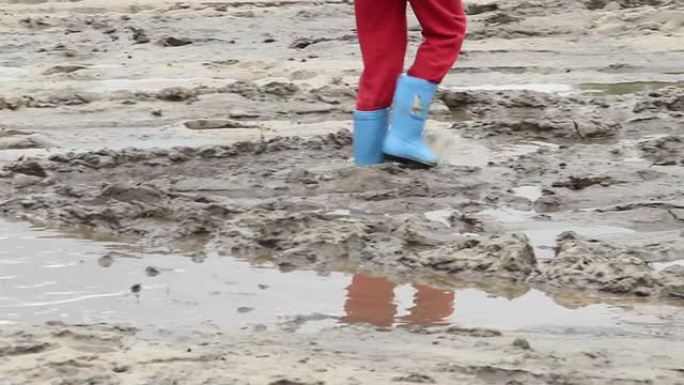儿童脚在水坑泥土上行走，蓝色靴子，儿童不安全
