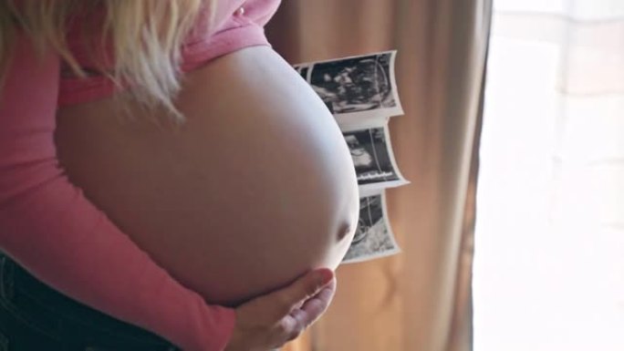 美丽的期待女人抚摸她怀孕的肚子和拿着超声波性别揭示她的宝贝孩子的照片，快乐的妈妈等待她心爱的孩子，美