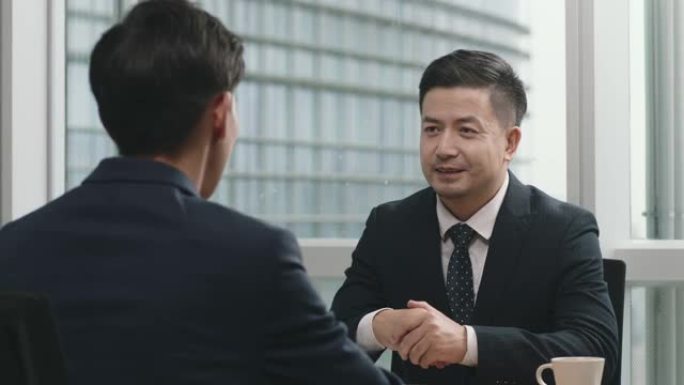 两名亚洲企业高管在办公室握手