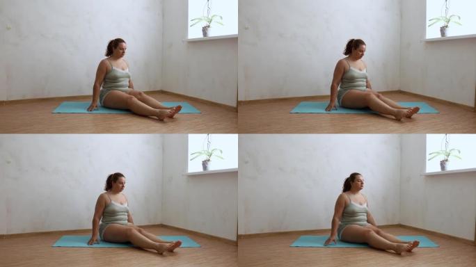 昏昏欲睡的超重女人坐在空荡荡的房间里的蓝色体操垫上，上下摇晃双腿，免费复制空间。家庭晨练，热身，运动