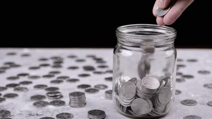 双手将一把累积的银币放入玻璃罐中。特写