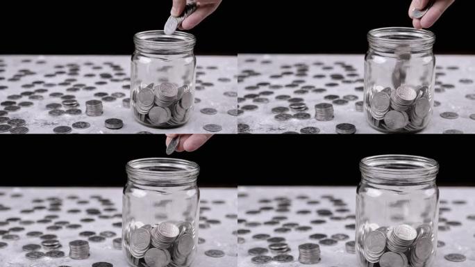双手将一把累积的银币放入玻璃罐中。特写
