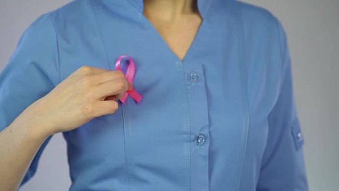 女医生将粉红丝带系在外套上，乳腺癌意识