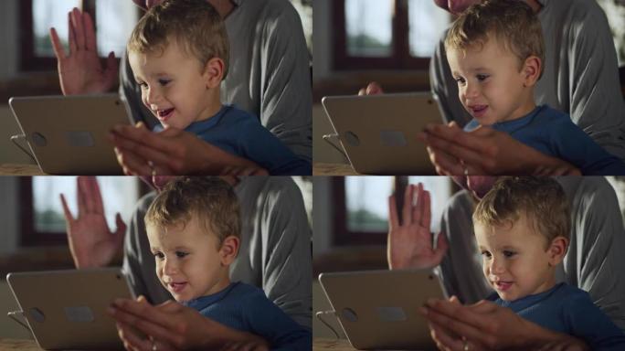 小男孩与母亲一起使用数字平板电脑拍摄的真实照片，他坐在家里的厨房里与家人进行视频通话。女人和她的儿子
