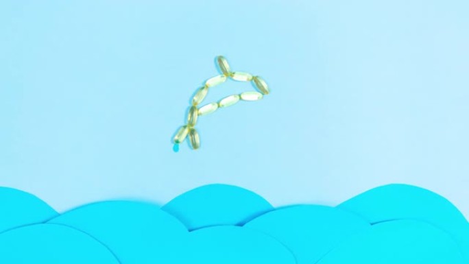 鱼由黄色透明胶囊制成，鱼油欧米茄3，从移动的蓝色波浪上方跳出海面。