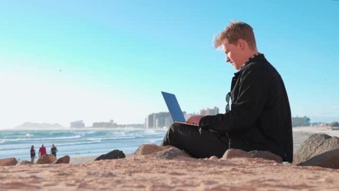 年轻人在海滩边缘附近使用笔记本电脑