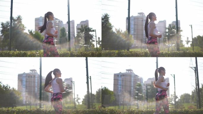 侧视图适合年轻的女运动员在阳光下慢动作地沿着网状栅栏奔跑。现场摄像机跟随苗条的白人运动女子在户外阳光