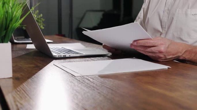 手拿商务文件，办公室木桌上的抽象文件，带笔记本电脑的桌子。文书工作概念。工作场所的商人