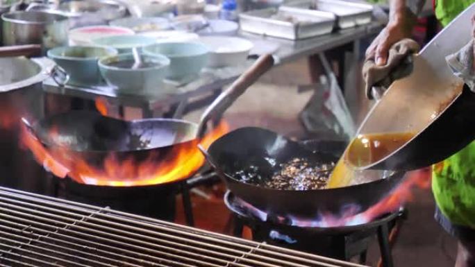 曼谷唐人街的街边炒锅大火。库克晚上在泰国Yaowarat路美食街市中心的马路上向外面的蔬菜燃烧热油。