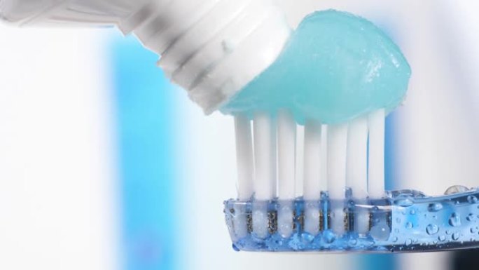 牙刷和牙膏。蓝色牙刷的宏观视图，上面有水滴，牙膏被挤压在蓝白色背景上，有复制空间。慢动作视图