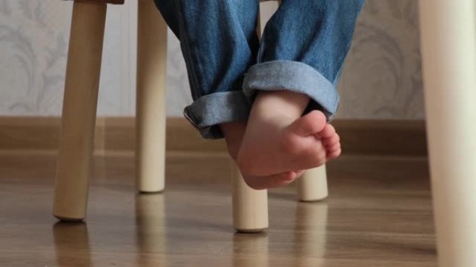 小迷人的孩子们的脚在椅子上跺脚。穿着牛仔裤的婴儿赤脚坐在椅子上，移动手指。
