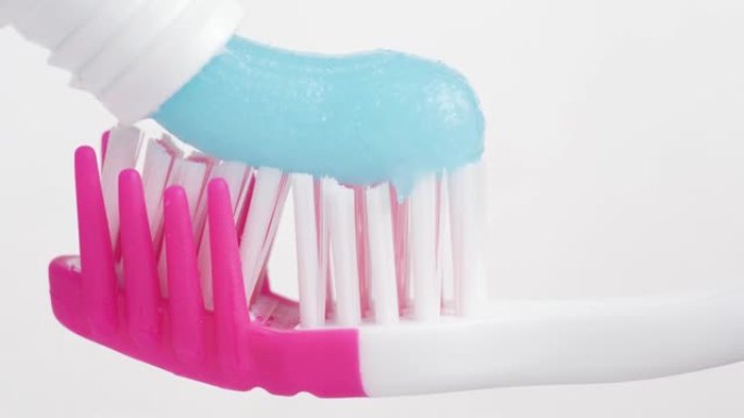 牙刷和牙膏。粉红色牙刷的宏观视图，白色背景上挤压蓝色牙膏。慢动作视图