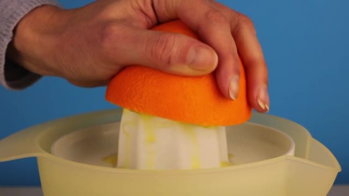 女人的手在电动榨汁机上榨取橙汁。