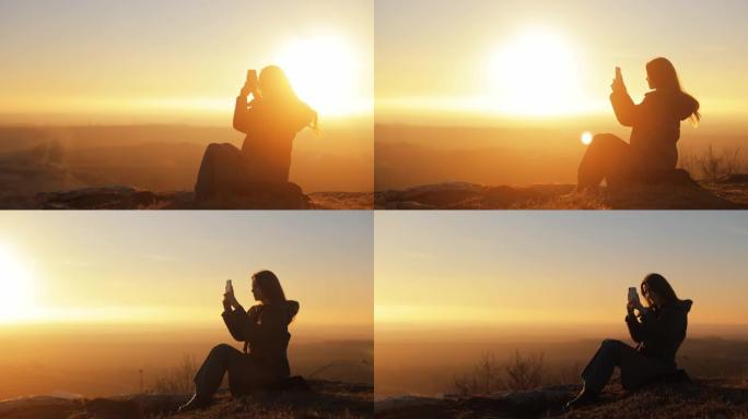 日落时，快乐微笑的女女孩在黄色天空下的剪影坐在山顶上，景色令人难以置信，并在手机摄像头、旅行者、户外