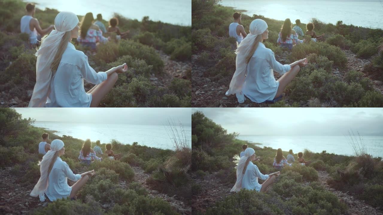 一群不同的朋友坐在蓝色大海边的草崖上，一起放松。莲花姿势冥想并练习健康